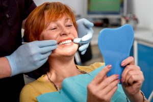 woman looking at pristine teeth while holding a mirror